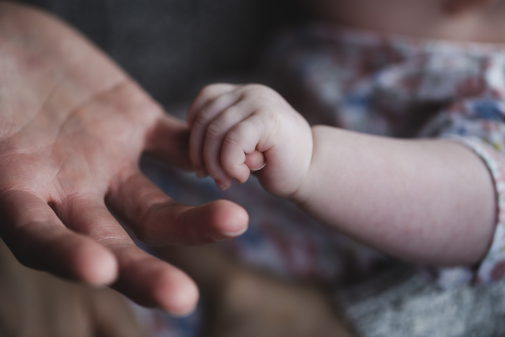 A small baby's hand holding an adult's finger